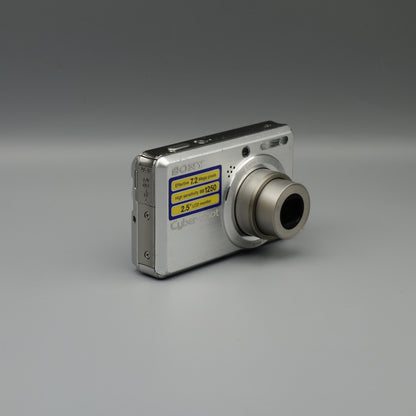Angled front view of a silver Sony Cyber-shot DSC-S750 showing its extended lens and yellow feature sticker
