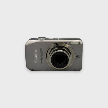 Front view of a silver Canon PowerShot SD4500 IS digital camera with its lens extended