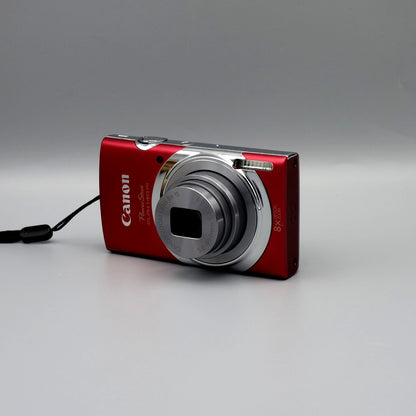 Red Canon PowerShot ELPH 140 IS viewed from the opposite front corner with its silver lens extended