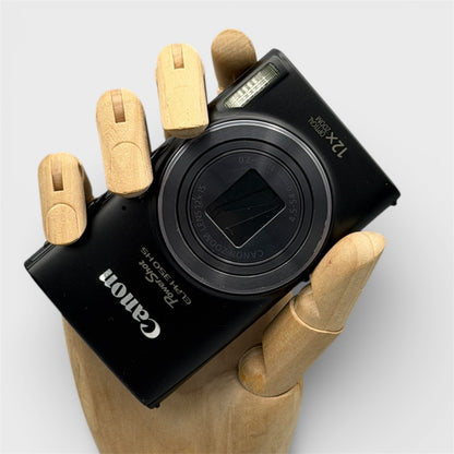 Black Canon PowerShot ELPH 350 HS digital camera resting in a wooden hand with the lens closed