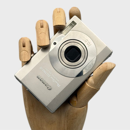 Silver Canon PowerShot SD790 IS digital camera resting in a wooden hand with the front visible