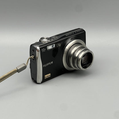 Angled front view of a black Fujifilm FinePix F70EXR with its lens extended and wrist strap attached
