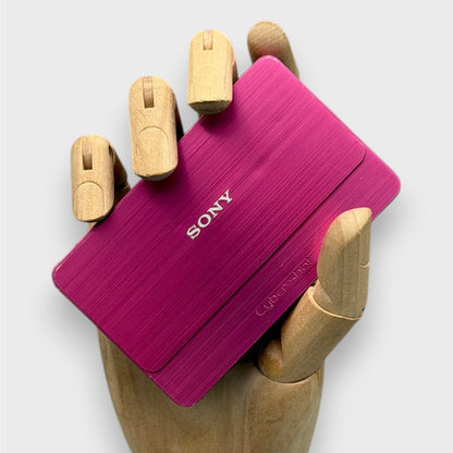 Pink Sony Cyber-shot DSC-T700 with its sliding lens cover closed, held in a wooden display hand
