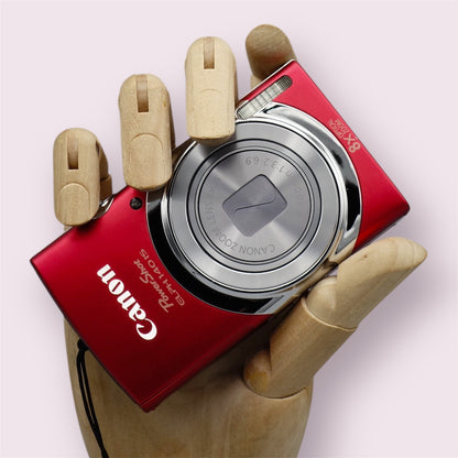 Red Canon PowerShot ELPH 140 IS with its lens closed, held in a wooden display hand
