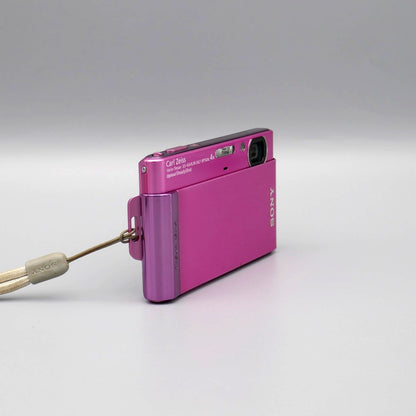 Angled front view of a pink Sony Cyber-shot DSC-T90 showing the exposed lens and top controls