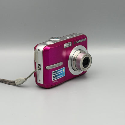 Angled front view of a pink Samsung S860 showing the extended lens and top controls