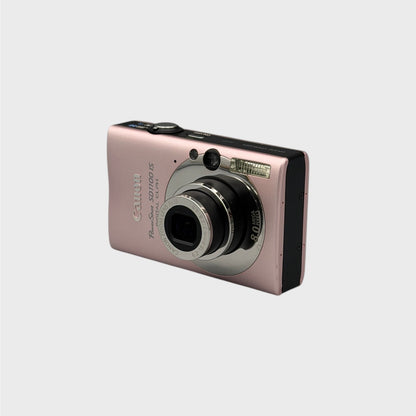 Pink Canon PowerShot SD1100 IS viewed from a front angle showing the extended lens and black side panel.