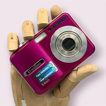 Pink Samsung S860 digital camera resting in a wooden hand with the lens closed