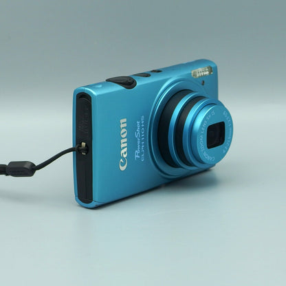 Angled front view of a blue Canon PowerShot ELPH 110 HS showing the extended lens and top controls