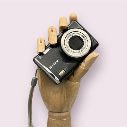 Black Fujifilm FinePix F70EXR digital camera resting in a wooden hand with the lens closed