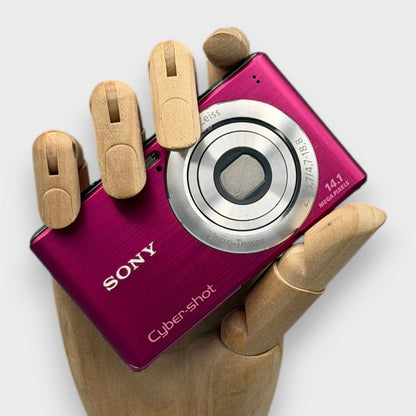 Pink Sony Cyber-shot DSC-W530 held in a wooden display hand with its lens closed.
