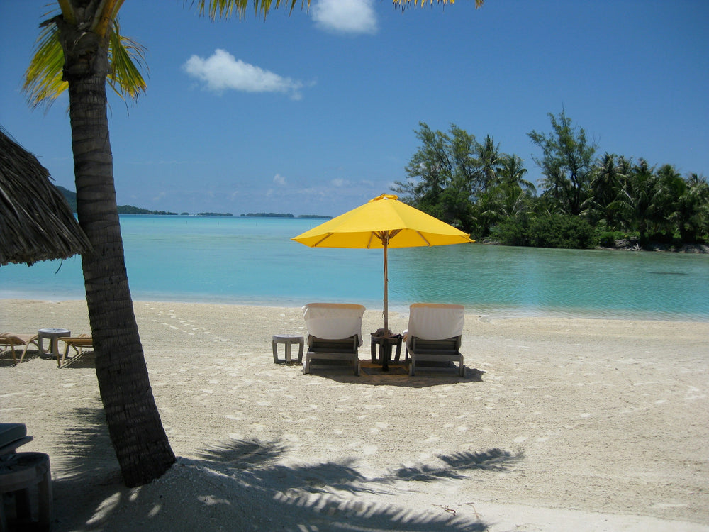 Two empty chairs beneath a yellow umbrella beside turquoise water