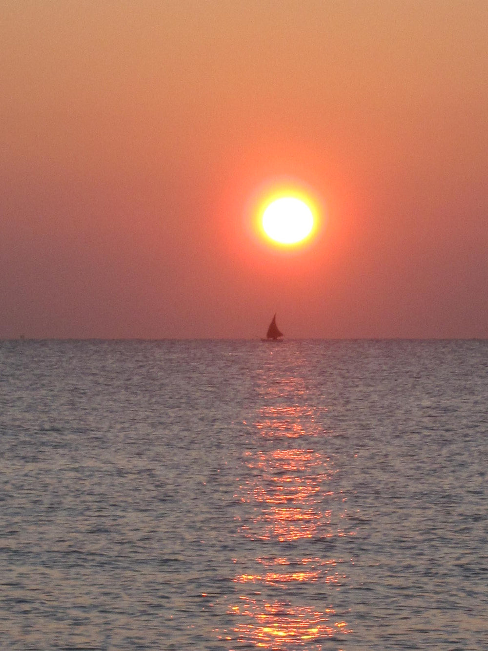 Orange sunrise and a distant sailboat on calm sea